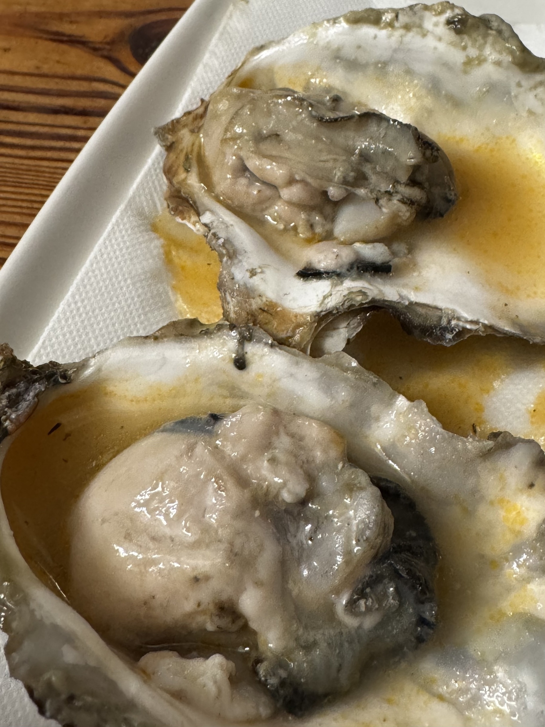 Two oysters served in their half shells on a white tray, dressed with an escabeche sauce that adds a light orange tint to the liquid around the oyster meat.