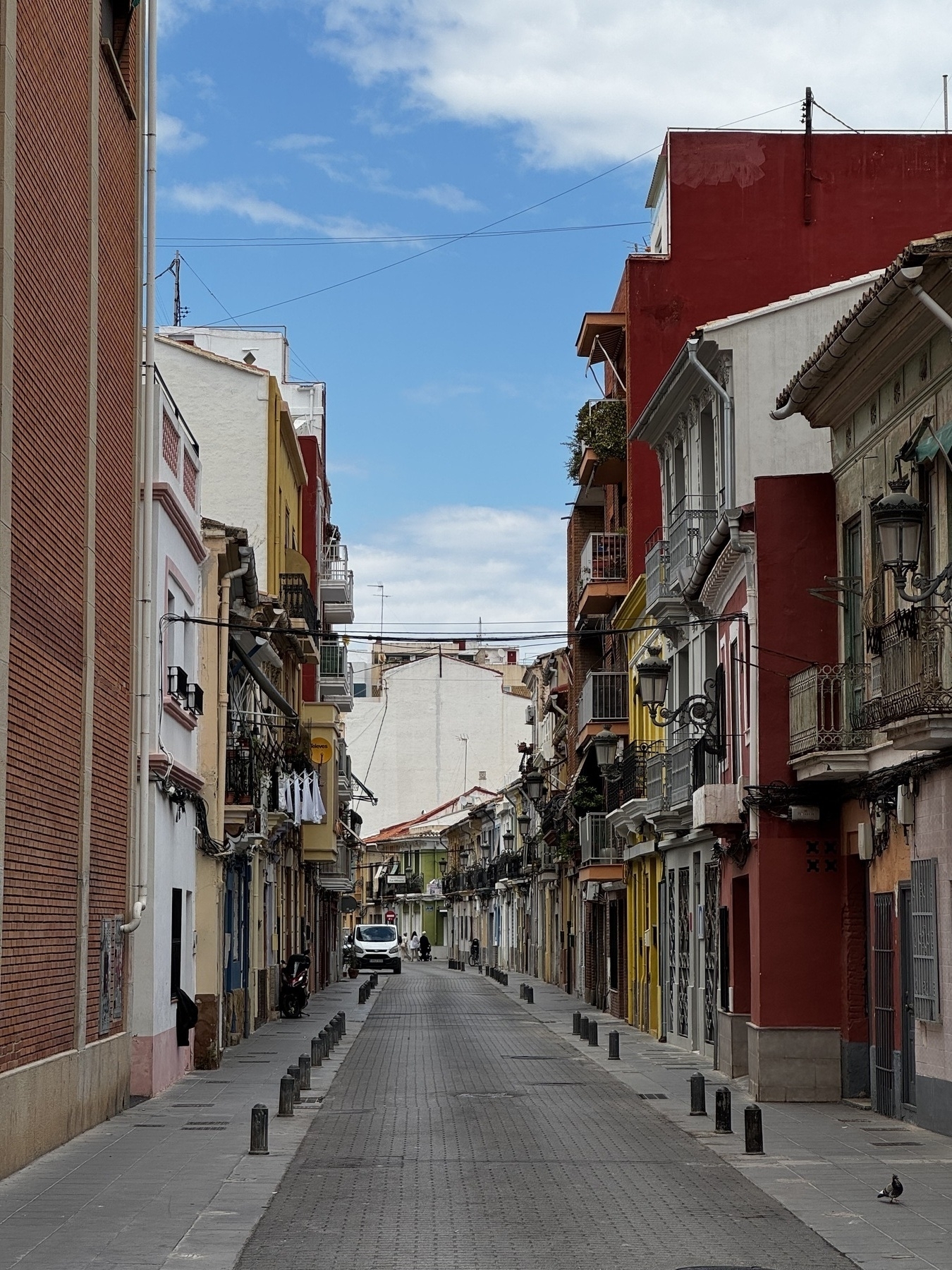A quiet residential street lined with narrow, colorful buildings creates a peaceful, intimate scene. The faded paint, balconies, and potted plants hint at daily life in a historic neighborhood untouched by time.