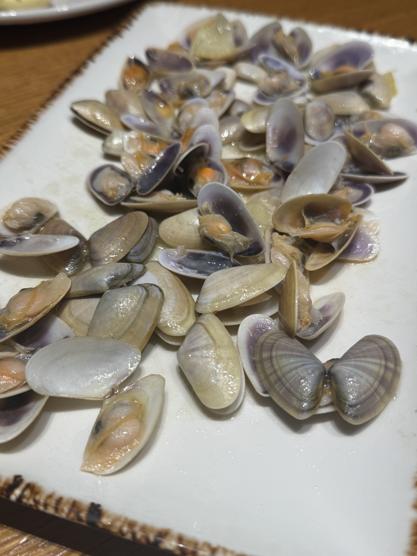 A plate is filled with many small, opened clams with visible insides.