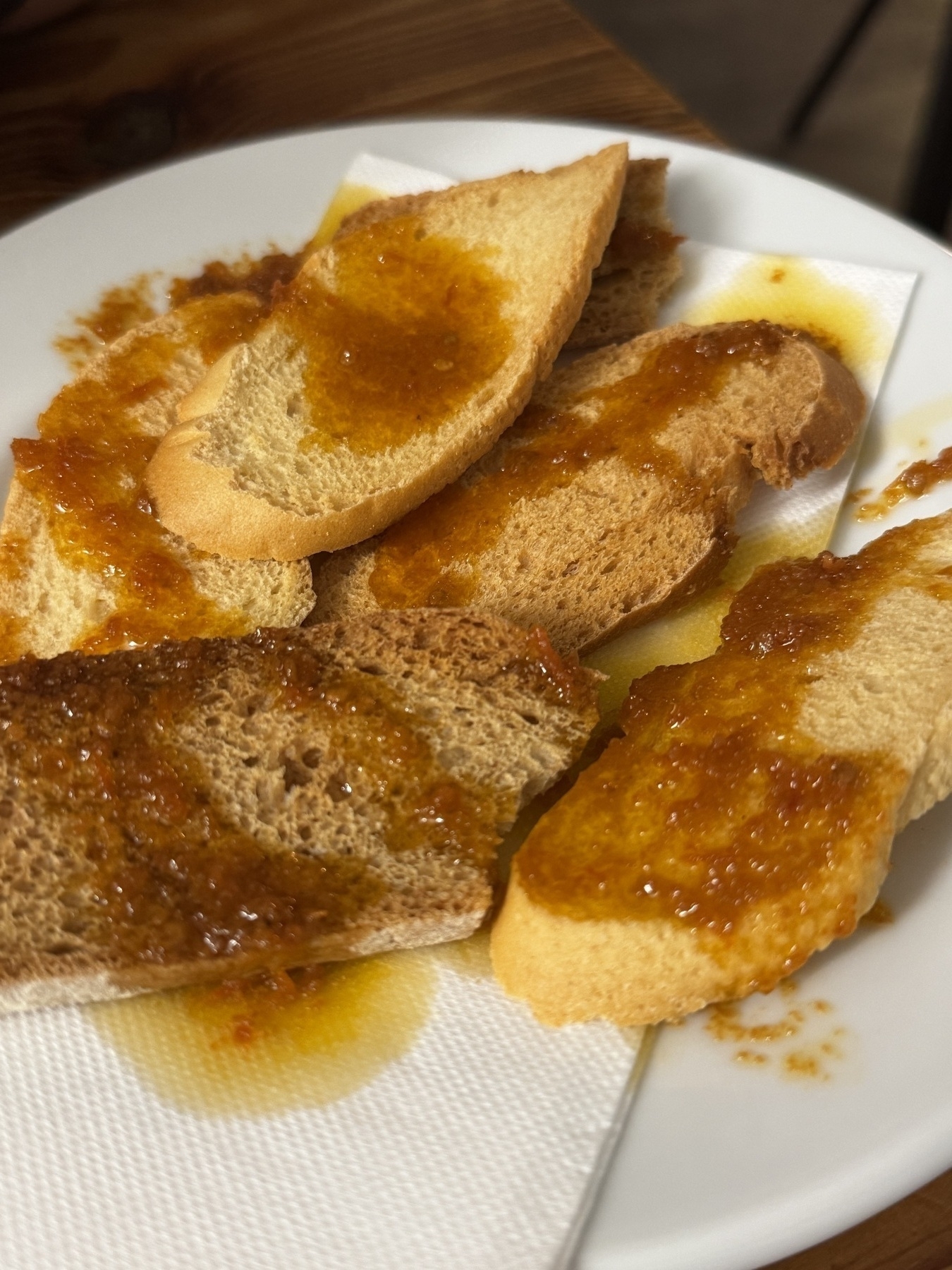 Several slices of toasted baguette on a white plate, generously topped with a rich tomato-based sauce. The plate is lined with a paper napkin underneath.