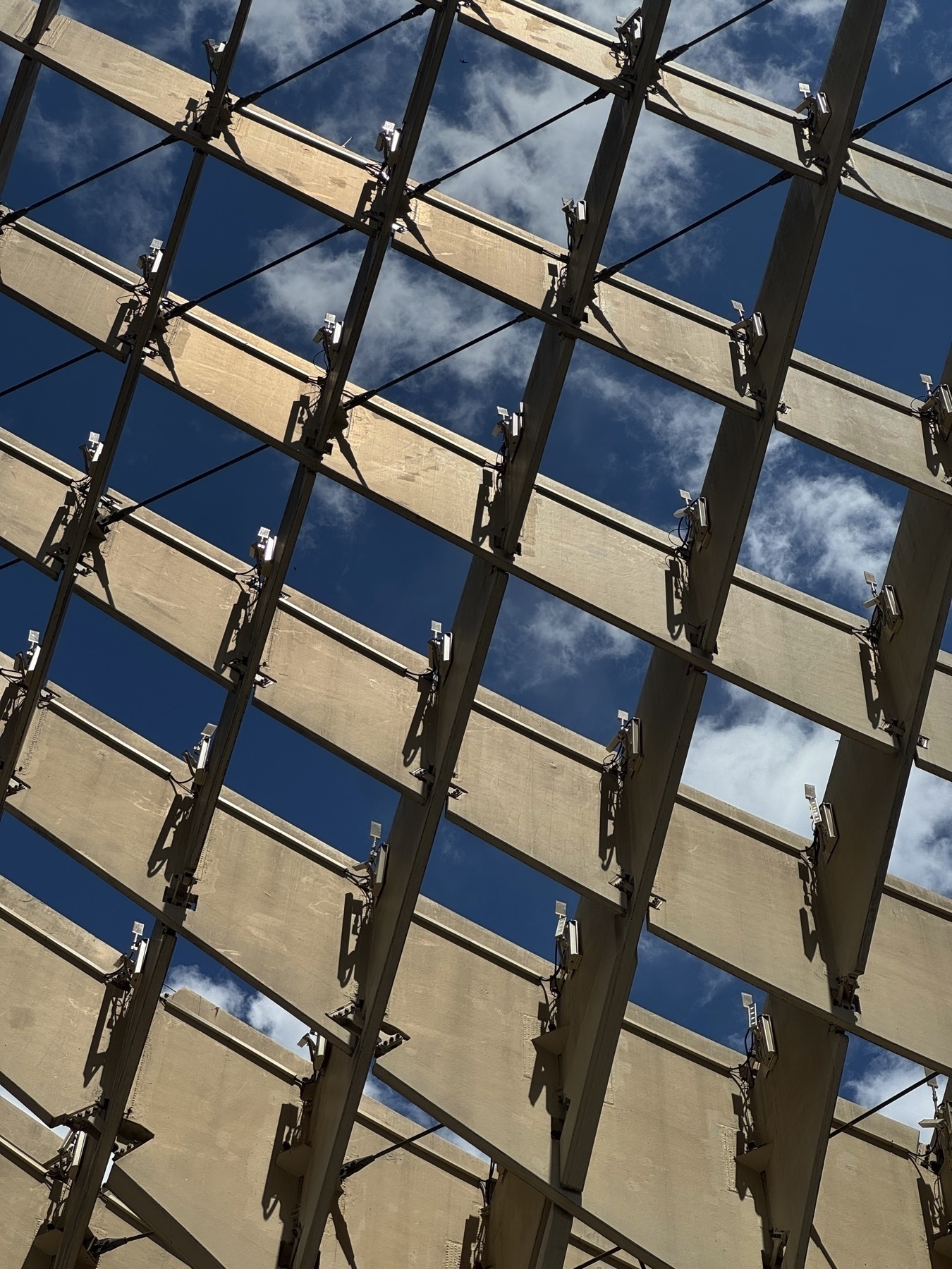 A close-up view of Metropol Parasol’s wooden grid structure, revealing the geometric pattern of panels and beams silhouetted against a vivid blue sky with scattered white clouds.