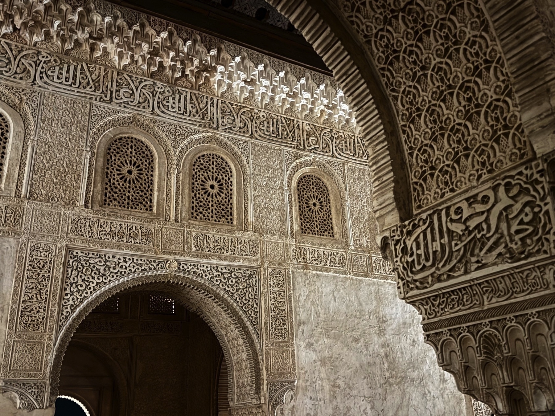 Detailed view of ornate stucco and calligraphic inscriptions in Arabic from a wall and archway inside the Nasrid Palaces, showcasing the fine craftsmanship of Islamic architecture at the Alhambra.