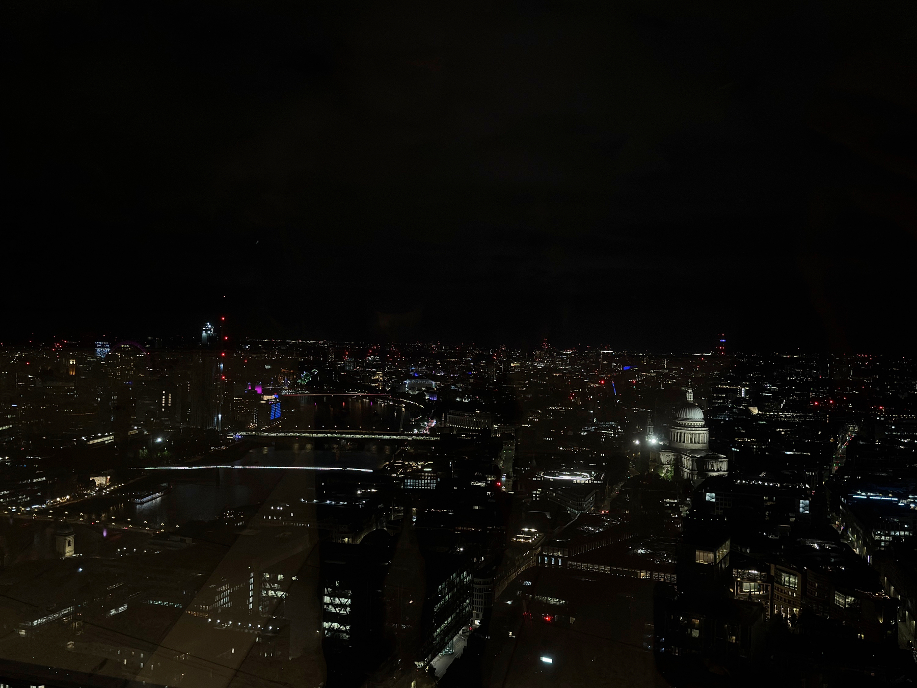 A sweeping nighttime panorama of London with the River Thames winding through the city and St Paul’s Cathedral glowing white among dense clusters of city lights.