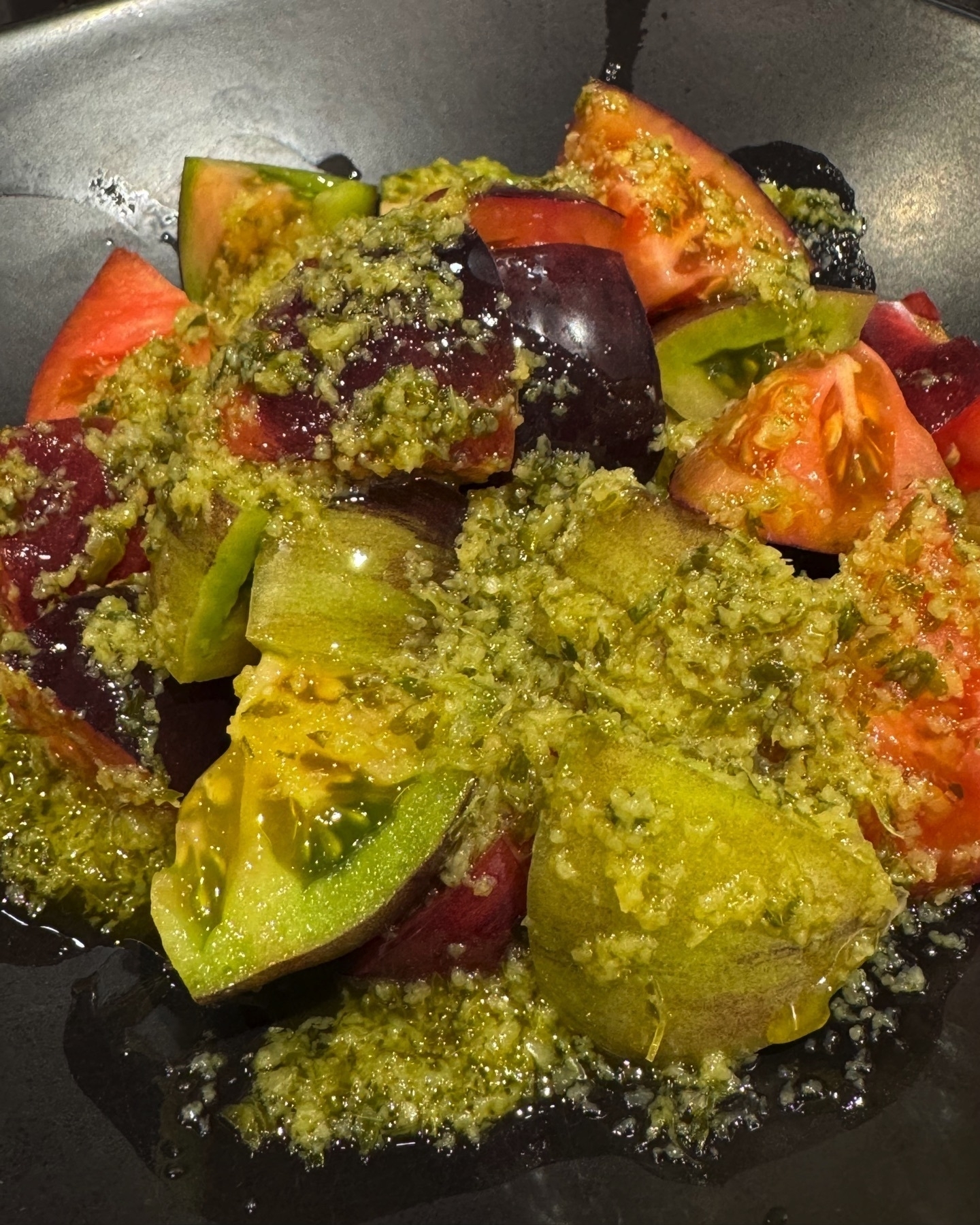 Heirloom tomato salad with a vibrant mix of red, purple, and green tomato wedges, generously drizzled with a bright green garlic and herb dressing. The tomatoes look juicy and ripe, and the chunky dressing gives a rustic, homemade appeal.