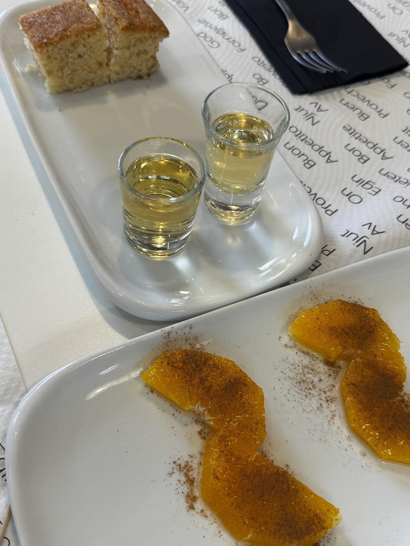 Dessert of orange slices with cinnamon, sponge cake, and two small glasses of sweet mistela wine.