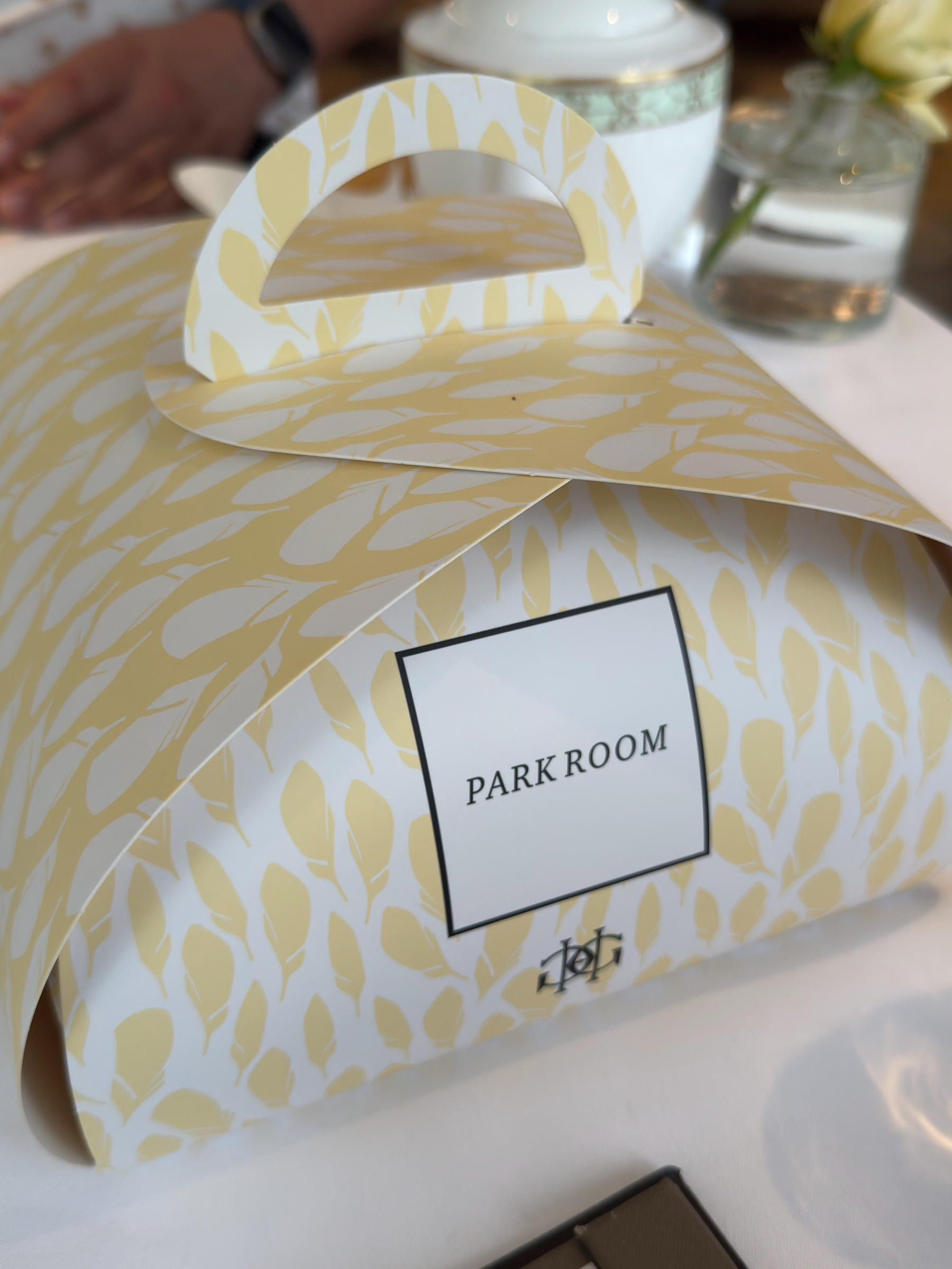 A patterned takeaway box labeled Park Room rests on the table, its soft yellow design echoing the tea set. It feels like a thoughtful, indulgent extra meant to extend the experience beyond the table.