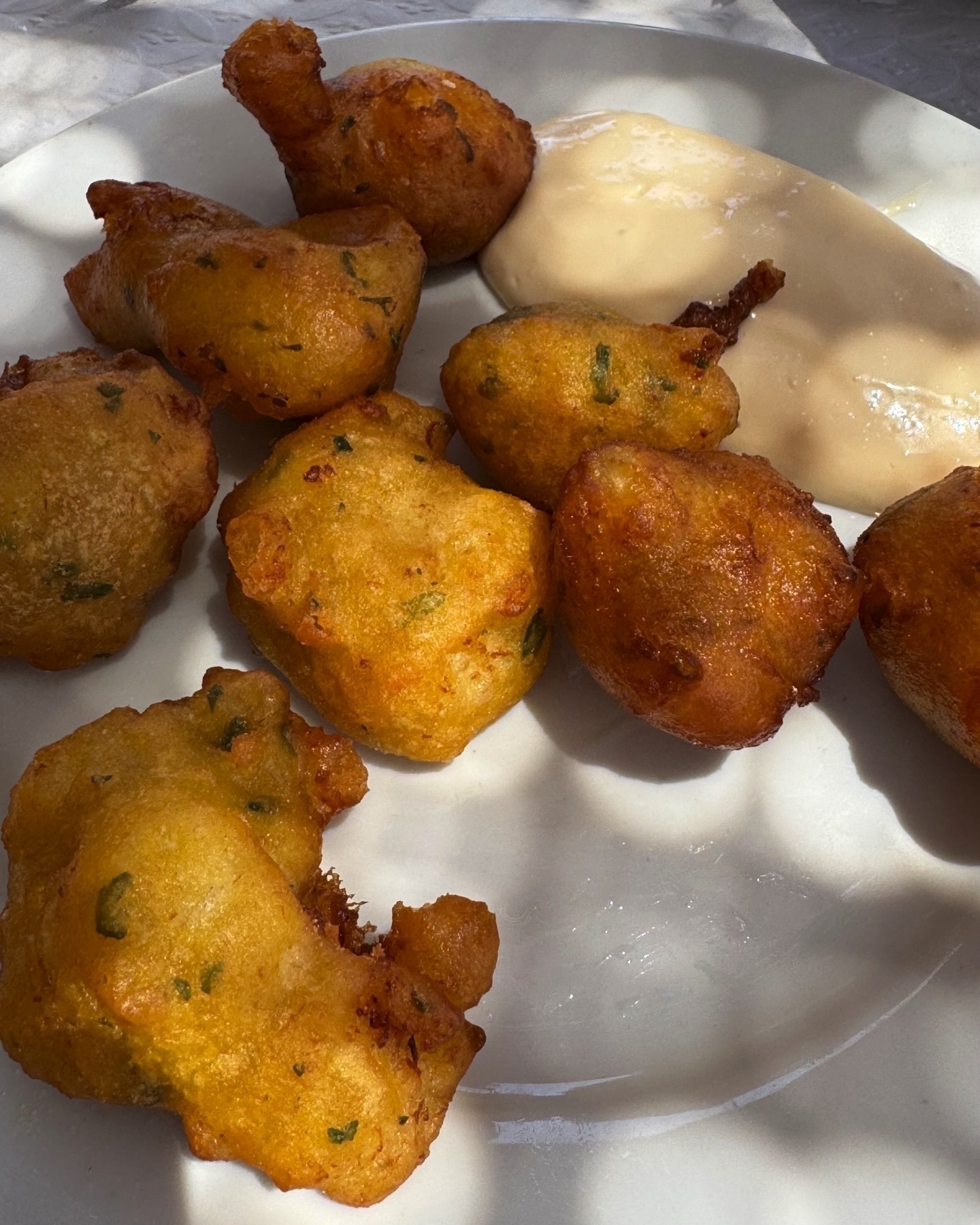 Plate of golden, crispy fried cod fritters speckled with green herbs, served with a generous dollop of smooth garlic aioli on the side.