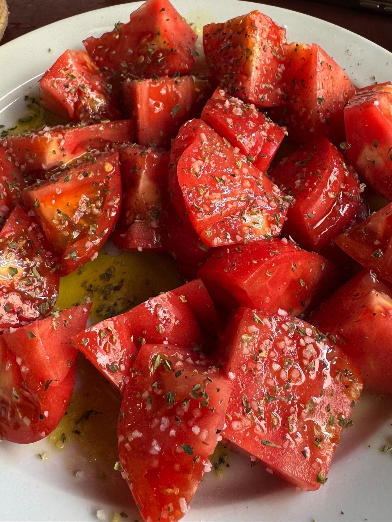 Plate of juicy, ripe tomato chunks generously seasoned with coarse salt, dried herbs, and drizzled with olive oil, enhancing the vibrant red color and fresh texture of the tomatoes.