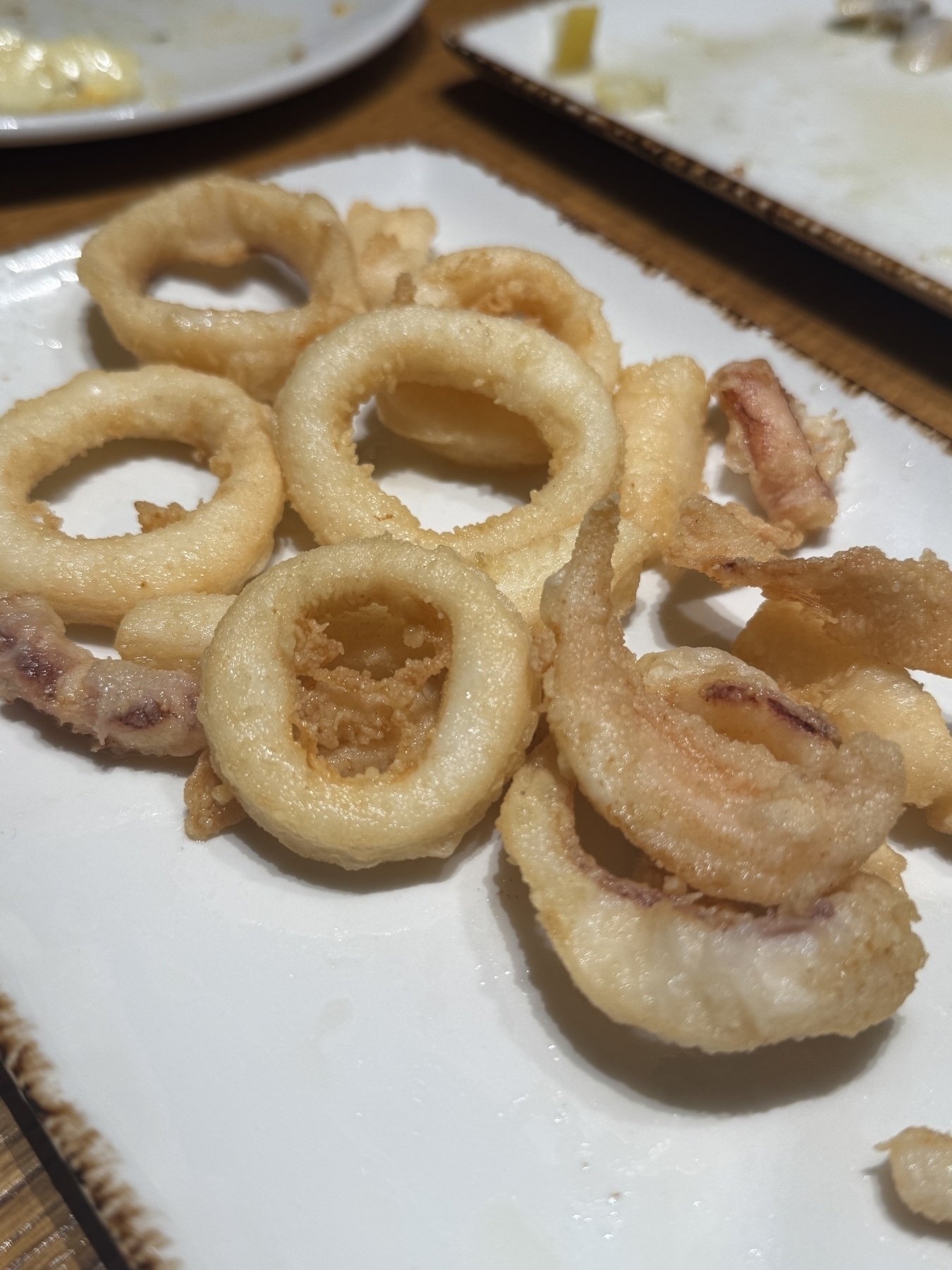 A plate of fried calamari rings is served on a rectangular dish.