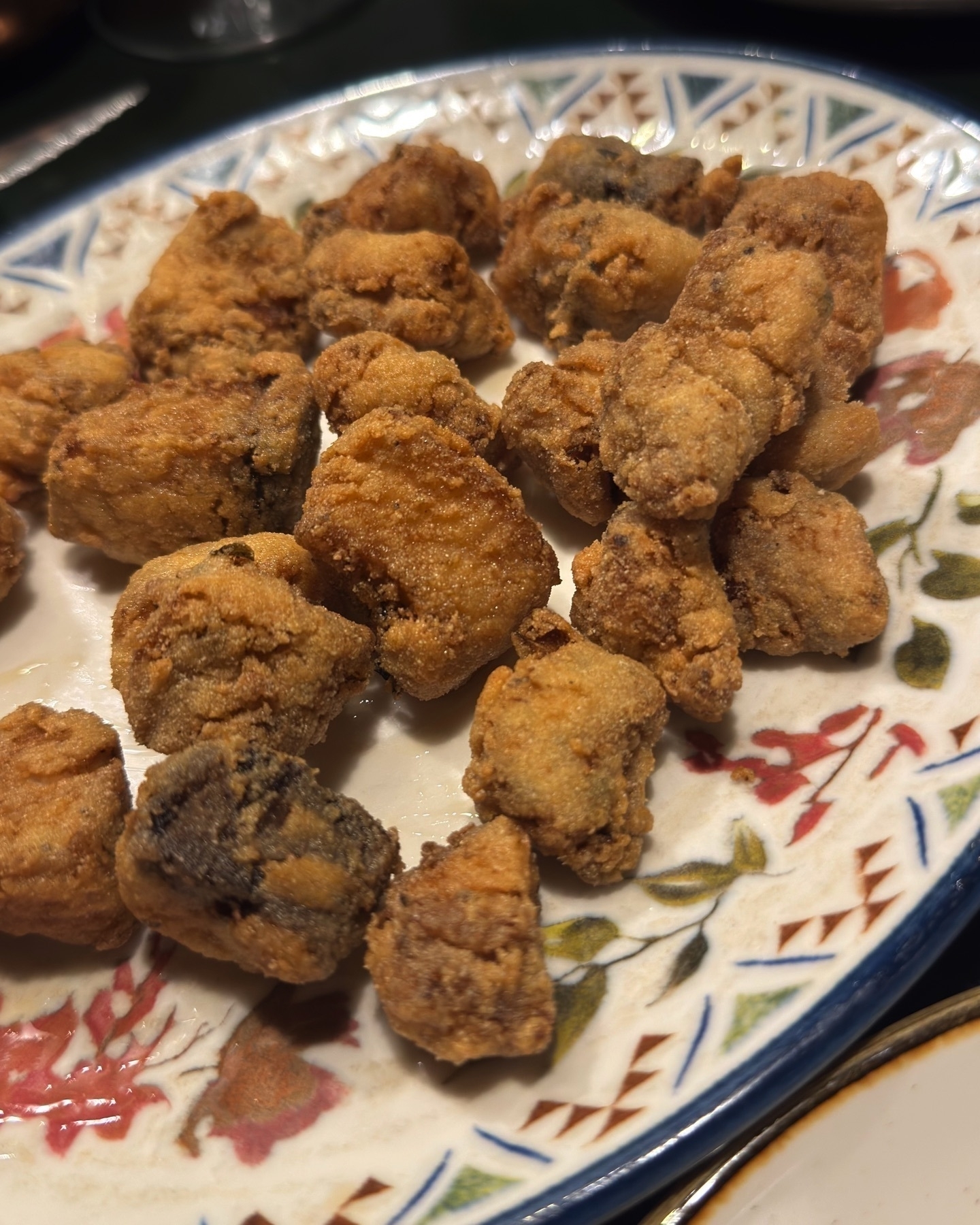 A plate of Adobo Sanluqueño, featuring bite-sized pieces of marinated dogfish coated in a light, golden batter and deep-fried to a crisp. The irregularly shaped pieces hint at a rustic, home-style preparation. Presented on a traditional Andalusian ceramic plate, the dish looks crunchy, savory, and inviting.