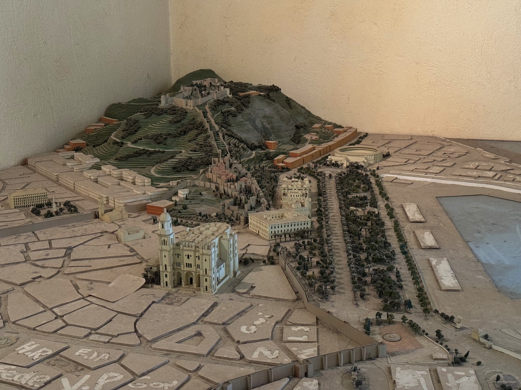 A detailed architectural scale model showing the layout of Málaga, featuring the hilltop fortress, historical buildings, and organized avenues lined with miniature trees. The model offers a top-down perspective with fine detail in terrain and structures.
