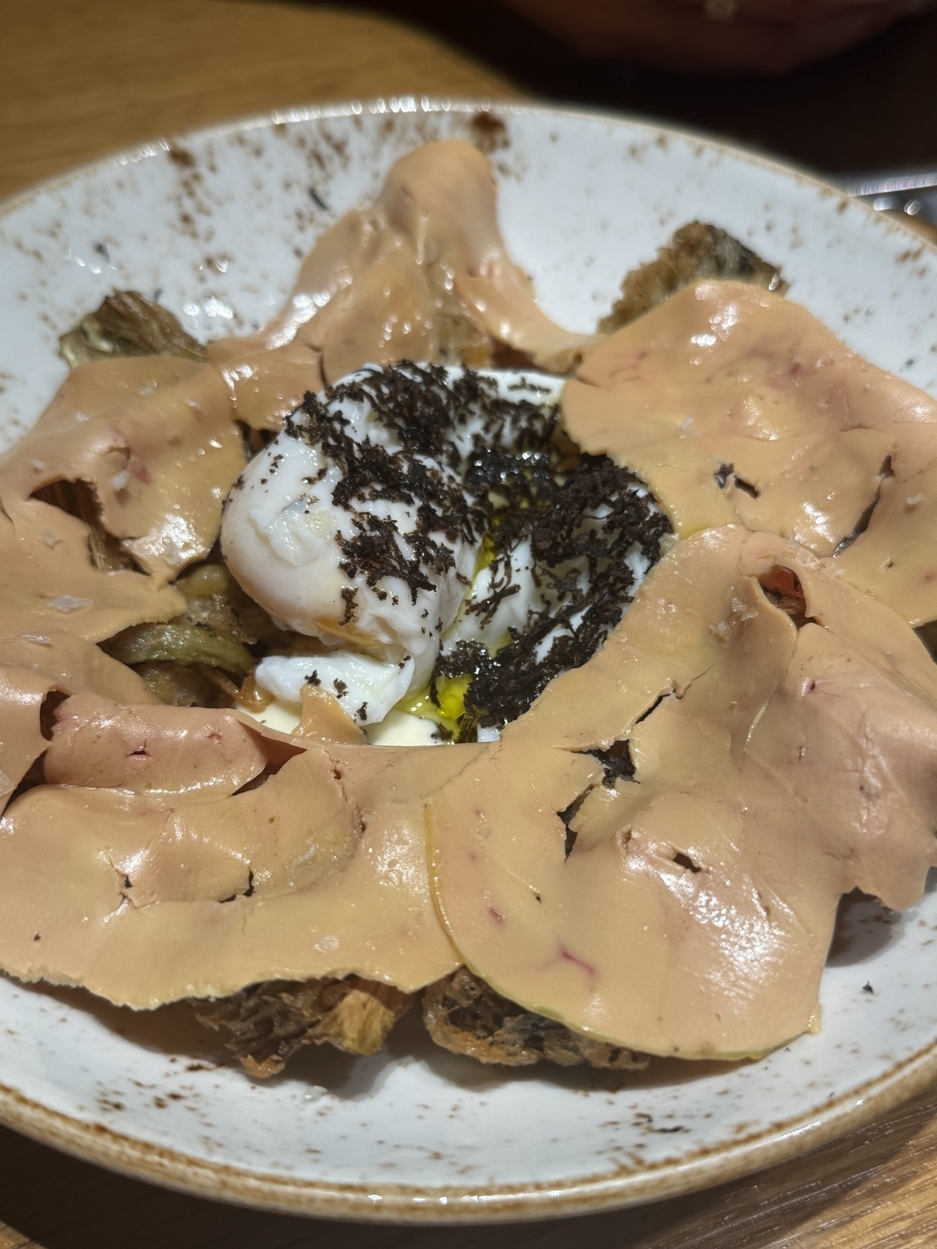 A plate features slices of cured meat surrounding a poached egg topped with grated truffle.