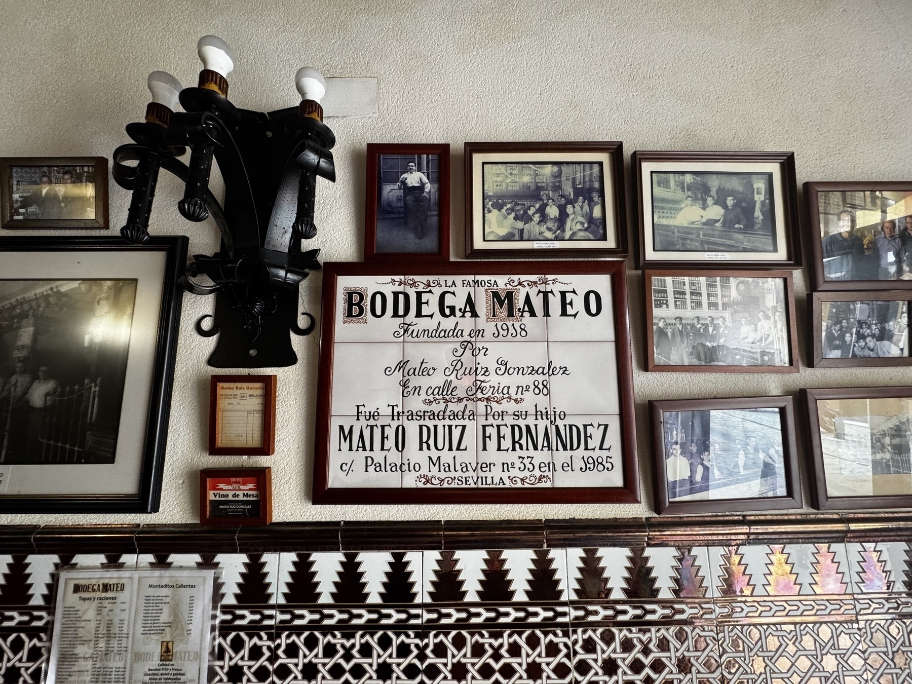 Wall inside the restaurant decorated with framed photographs and a central sign detailing the history of Bodega Mateo, founded in 1938.