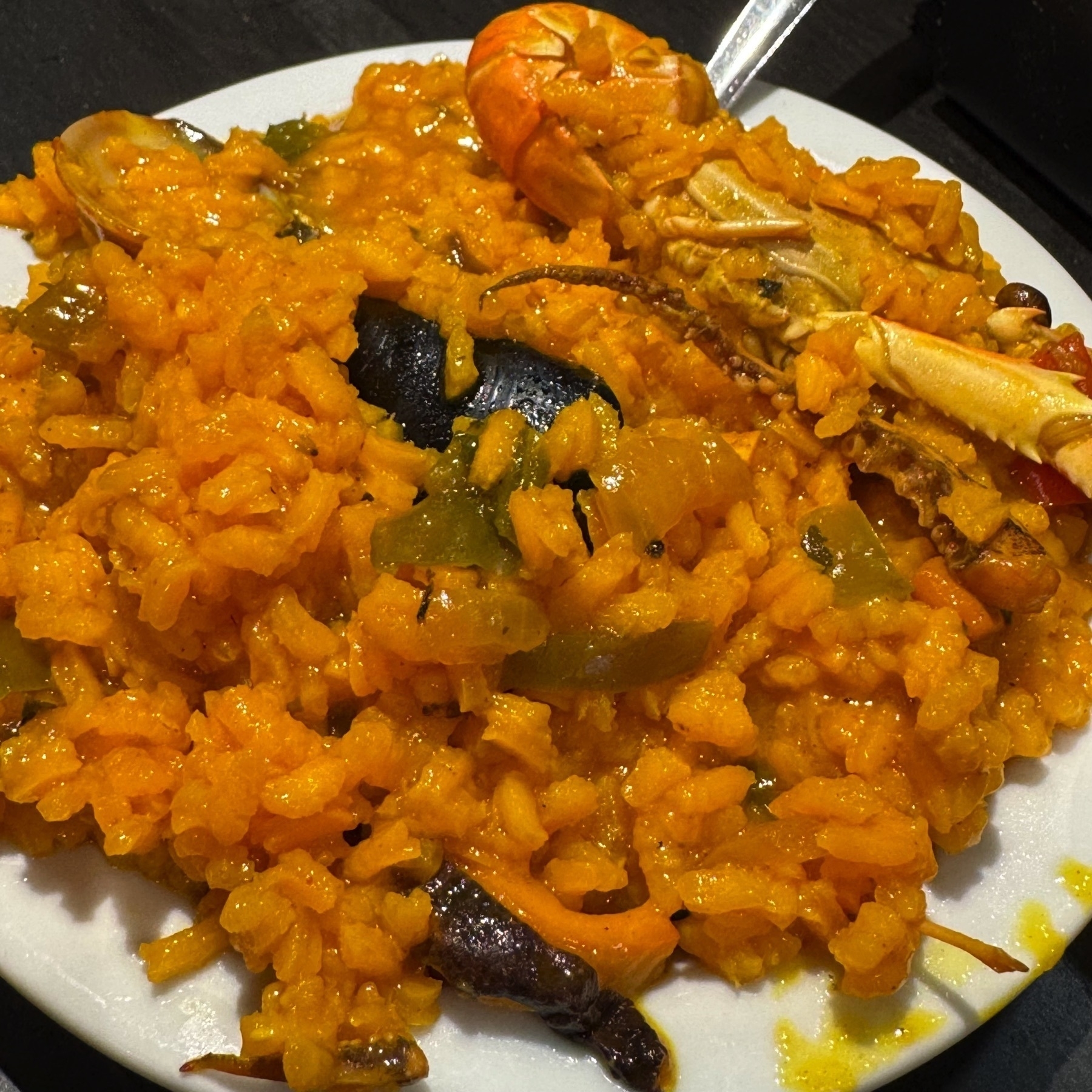 A heaping plate of seafood paella with vivid golden-yellow rice, generously studded with green bell pepper, shell-on prawns, mussels, and a langoustine. The rice appears moist and glossy, capturing the essence of a well-made sofrito and rich seafood stock.