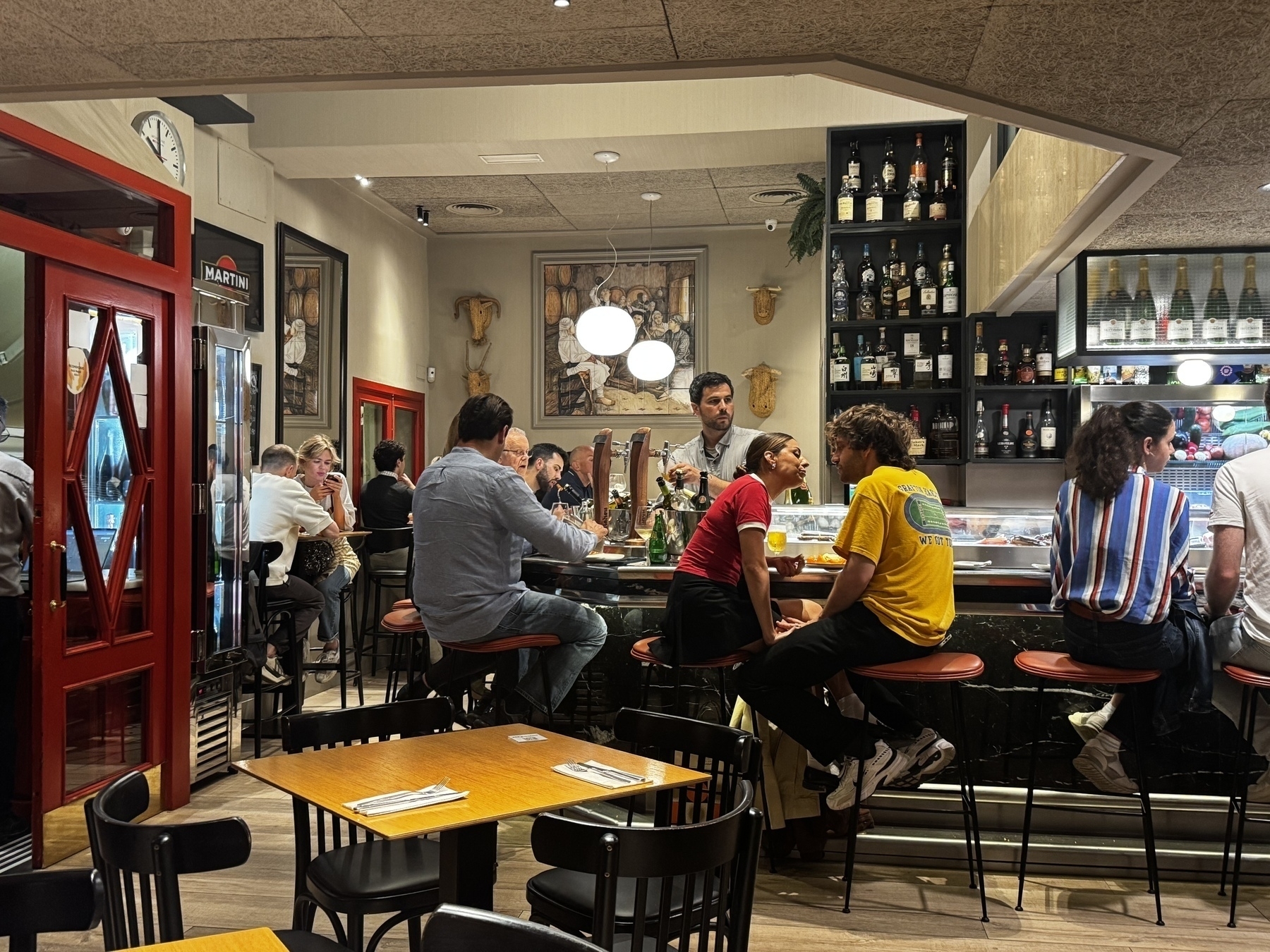A lively restaurant and bar with patrons seated at the counter and tables, engaging in conversation.